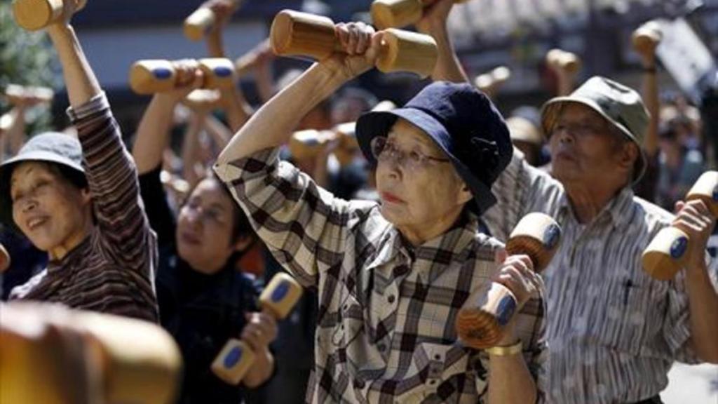 Ancianos japoneses realizan ejercicio con mancuernas de madera.